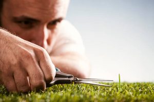 A man trimming an blade of grass that's slightly above the level of the rest of the lawn